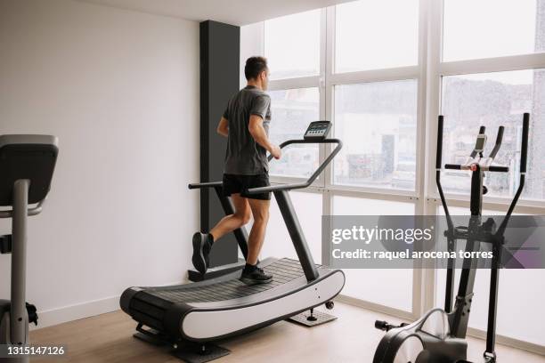 caucasian adult man running on a treadmill in the gym next to a large window - running on treadmill stock pictures, royalty-free photos & images