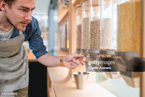 male employee checking the stock in cereal dispensers in a sustainable store - change dispenser stock pictures, royalty-free photos & images