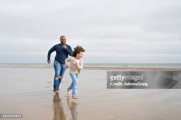 british father and young daughter playing at camber sands - candid beach stock pictures, royalty-free photos & images