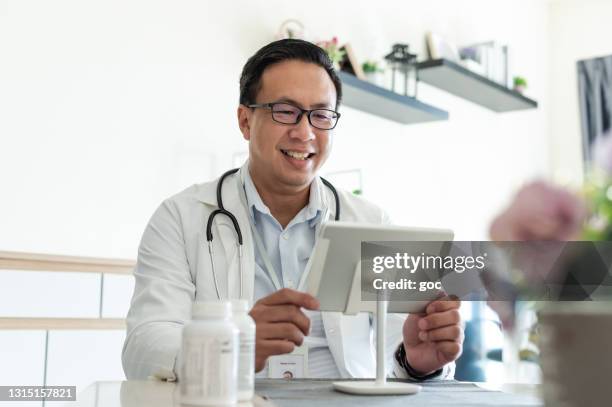 asian male doctor consulting and consoling his patient on live video call at hospital clinic - telemedicine male stock pictures, royalty-free photos & images