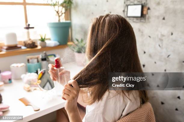 mujer joven usando spray para el cabello en el dormitorio temprano en la mañana - botella para rociar fotografías e imágenes de stock