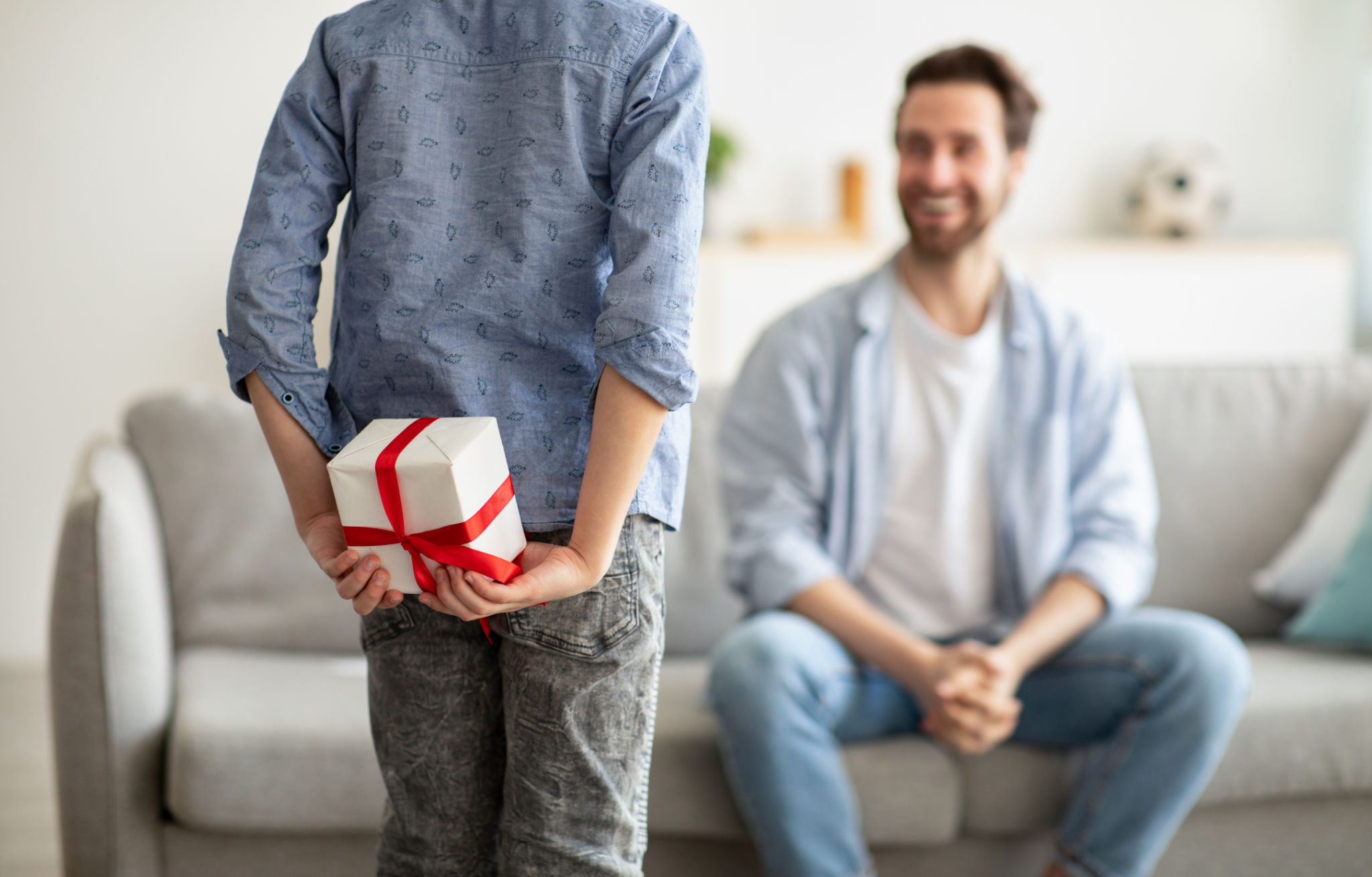 Boy greeting his young dad with Father's Day, hiding gift box behind his back, selective focus Boy greeting his young dad with Father's Day, hiding gift box behind his back, selective focus