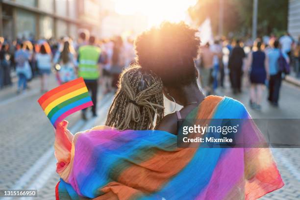 young female couple hugging with rainbow scarf at the pride event - dreadlocks back stock pictures, royalty-free photos & images
