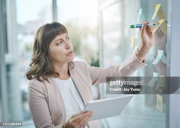 shot of a young businesswoman using a digital tablet during a brainstorming session in a modern office - transparent wipe board stock pictures, royalty-free photos & images