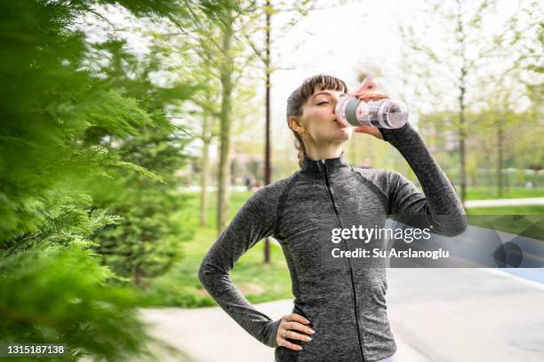 young female athlete drinking water after training in public park - tracksuit jacket stock pictures, royalty-free photos & images