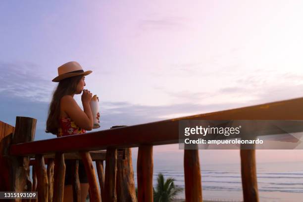 reopening hotel concepts - young latin female having an alcoholic cocktail at the hotel balcony on her vacations after corona virus pandemic illness with a beach seaside view during the sunset - ecuador landscape stock pictures, royalty-free photos & images