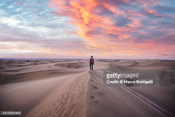 one man standing on top of a sand dune at sunrise, grand canary, spain - maestosità foto e immagini stock