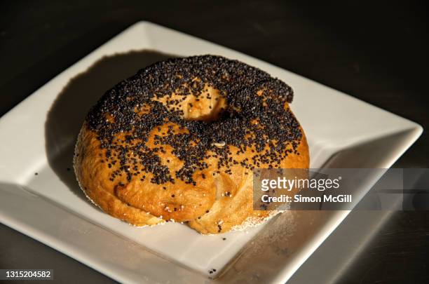 poppy seed and sesame seed bagel on a square white plate - poppy seed stock pictures, royalty-free photos & images
