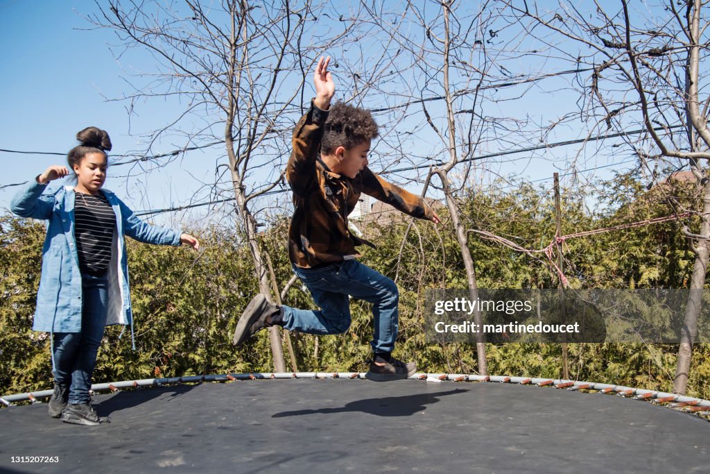 Siblings jumping on trampoline outdoors in springtime.