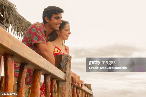 reapertura de los conceptos del hotel - joven pareja latina que se divierte juntos alojándose frente a la playa y mirando el paisaje desde su habitación de hotel balcón en sus vacaciones de luna de miel después de la enfermedad pandémica del virus cor - beach house balcony fotografías e imágenes de stock