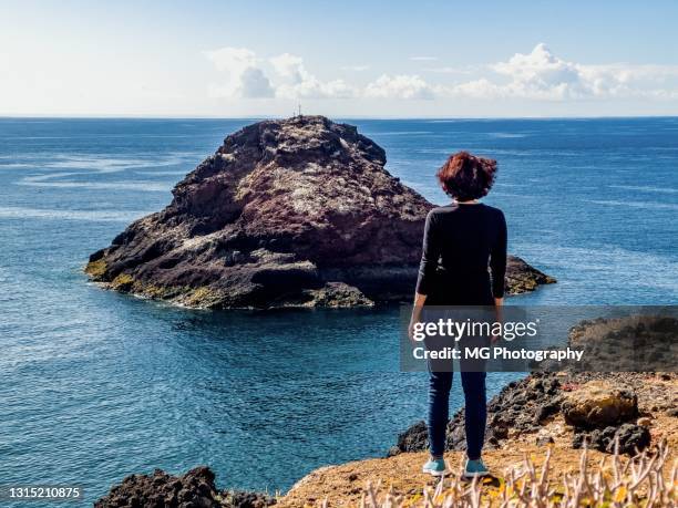 バックパックを持つ観光客の女性は、火山島を探して海岸に立っています - the castaway ストックフォトと画像