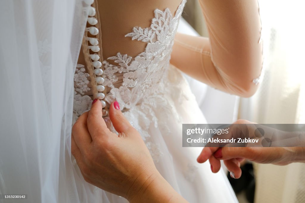 Mom laces up the back of her daughter's openwork stylish wedding dress. Morning Preparations of the bride, support and care of the mother.