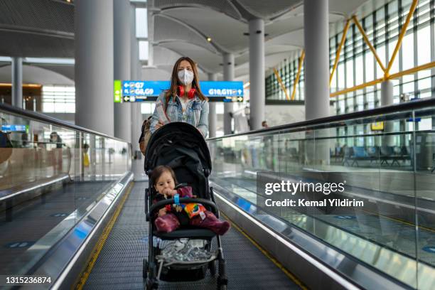 junge frau mit ihrem baby unterwegs, trägt eine gesichtsmaske während der covid-19 - toddler at airport stock-fotos und bilder