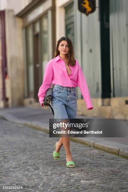 Alexandra Pereira wears a neon pink open oversized shirt from The Frankie Shop , a Dior Bobby monogram print bag, blue denim ripped shorts from Zara,...