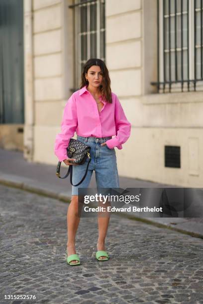 Alexandra Pereira wears a neon pink open oversized shirt from The Frankie Shop , a Dior Bobby monogram print bag, blue denim ripped shorts from Zara,...