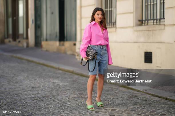 Alexandra Pereira wears a neon pink open oversized shirt from The Frankie Shop , a Dior Bobby monogram print bag, blue denim ripped shorts from Zara,...