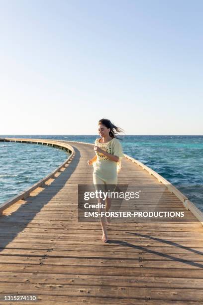 beautiful women is running on a very long jetty while sunrise leading into a red sea reef. - frau kleid stock-fotos und bilder