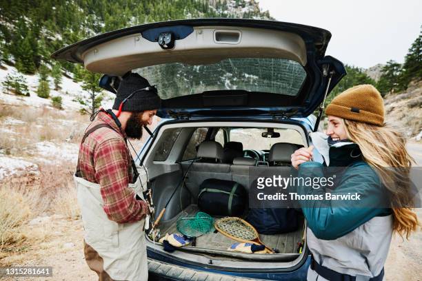 medium shot of couple at back of car preparing to go fly fishing on winter afternoon - thomas teal stock pictures, royalty-free photos & images