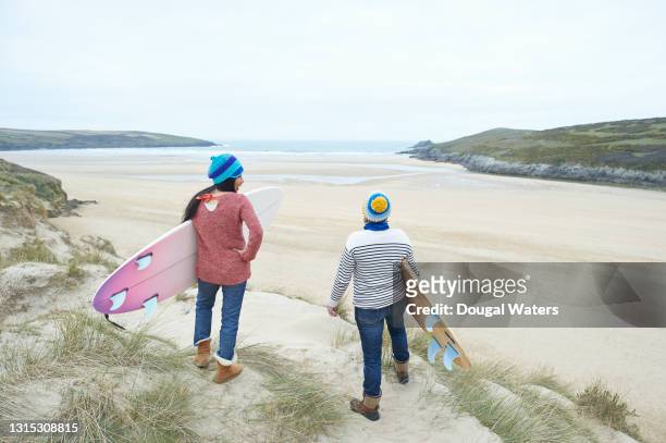 female surfers with surfboards looking out to sea. - couple dunes stock-fotos und bilder
