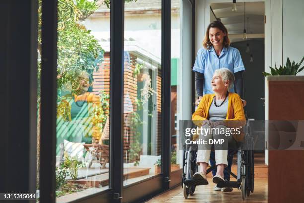 schuss einer jungen krankenschwester, die eine seniorin im rollstuhl in einem altersheim schubst - care stock-fotos und bilder