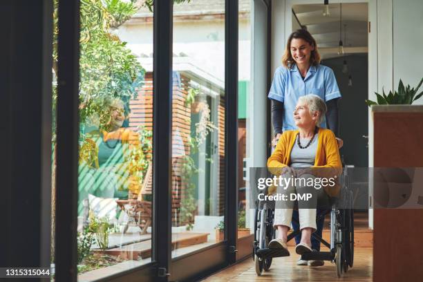 ontsproten van een jonge verpleegster die een hogere vrouw in een rolstoel in een bejaardentehuis duwt - treatment stockfoto's en -beelden