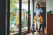 Shot of a young nurse pushing a senior woman in a wheelchair in a retirement home