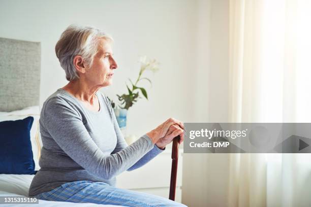 shot of a senior woman looking thoughtful while holding a walking stick at home - alzheimers disease stock pictures, royalty-free photos & images