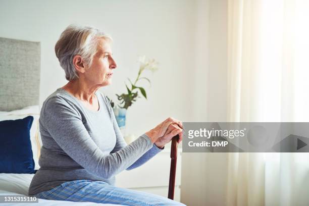 shot of a senior woman looking thoughtful while holding a walking stick at home - só uma mulher idosa imagens e fotografias de stock