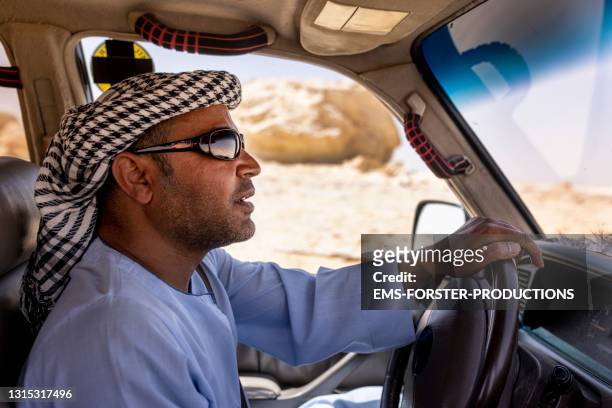 middle eastern man wearing traditional clothes driving off road vehicle in white desert - road to war in middle east and north africa stock-fotos und bilder