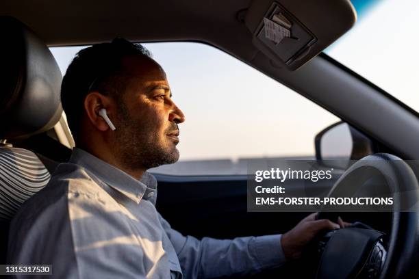 business man using ear pods while driving a car - arab driving stock-fotos und bilder