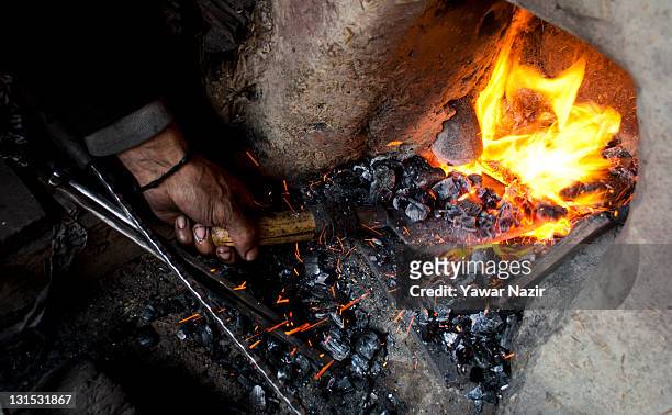 Kashmiri Muslim blacksmith heats up a knife in charcoal before shaping it in his workshop on November 05, 2011 in Srinagar, the summer capital of...