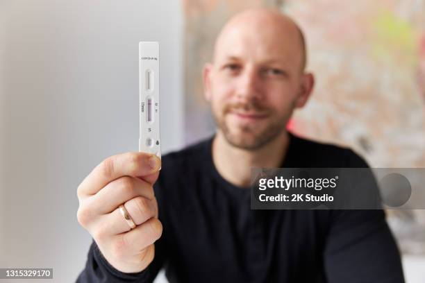 a young man is holding a negative rapid corona test or antigen test in his hand and pointing it towards the camera - antibody testing stock pictures, royalty-free photos & images