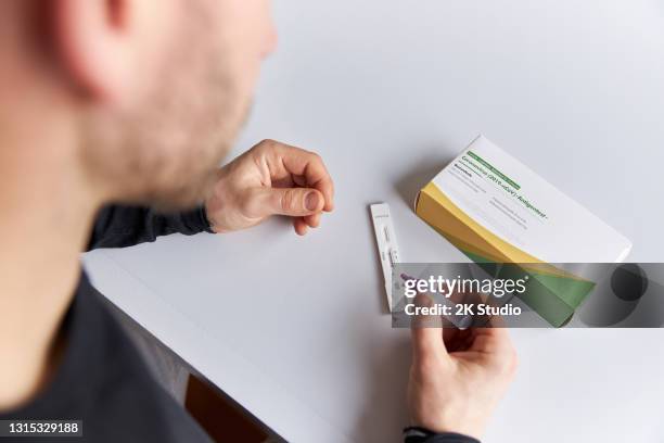 uma foto de perto de uma mão masculina fazendo um teste rápido de corona ou teste de antígeno em uma mesa branca. - teste de diagnóstico rápido - fotografias e filmes do acervo