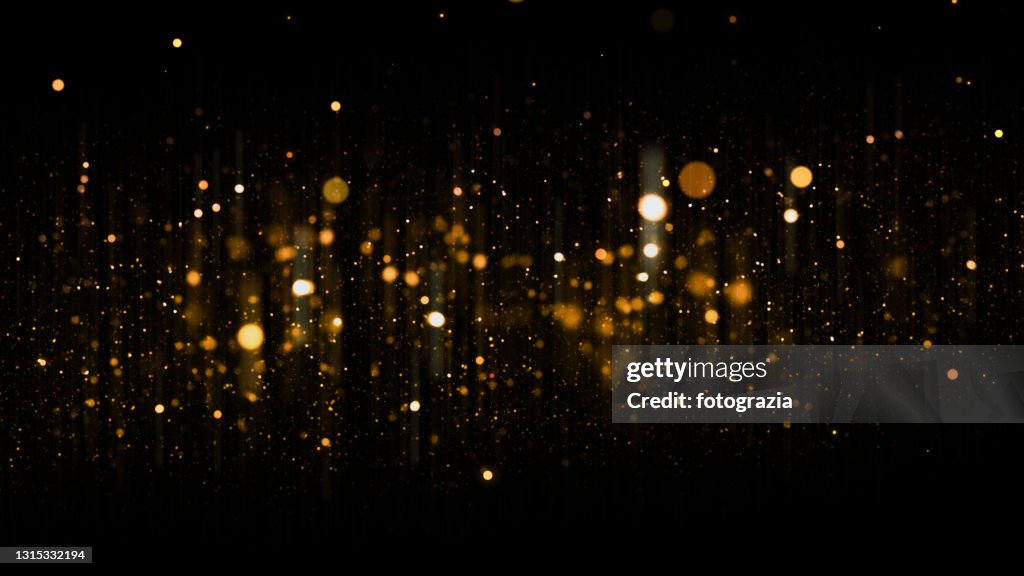 Defocused Golden Particles Glittery against Dark Background with Copy Space. Christmas Overlay