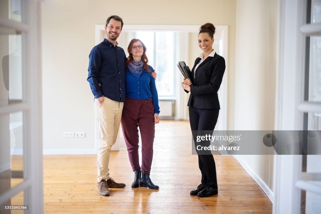 Casal sorridente em pé com agente imobiliário em nova casa