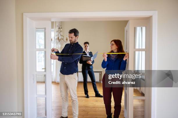 man and woman measuring new home doorway with tape while real estate agent watches - flat inspection stock pictures, royalty-free photos & images