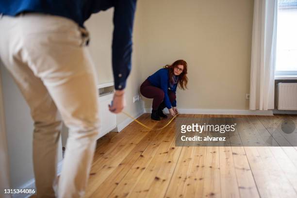 vrouw die terwijl het meten van vloer van nieuw huis met mens hurkt - huurhuis stockfoto's en -beelden