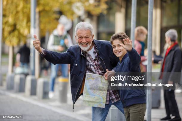 an older man and his grandson are standing in the street and waving with arms to catch a taxi. - taxi boys stock pictures, royalty-free photos & images