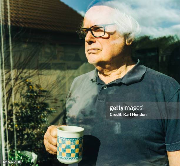 a mature man looks out of a window onto a back garden - stock photo - stuck in the past stock pictures, royalty-free photos & images
