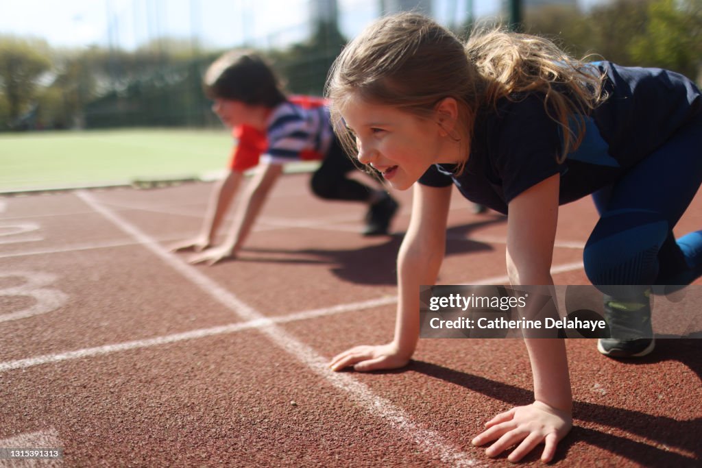 Young girl and boy ready to race on an athletics track