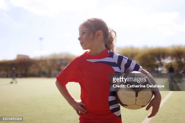 A young girl posing with a ball on a soccer field