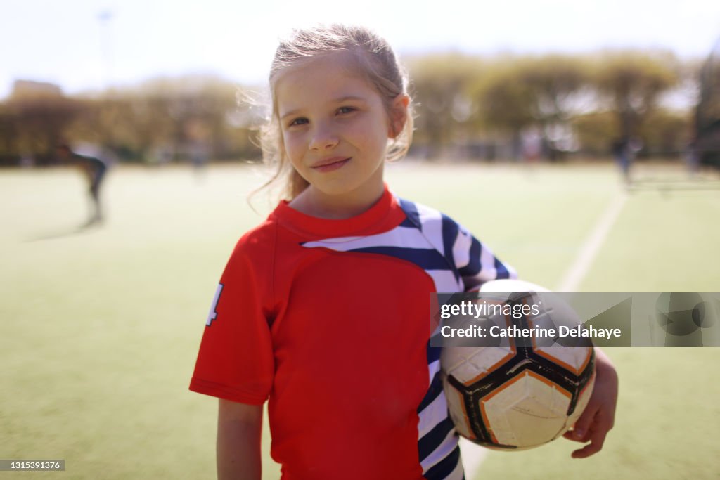 A young girl posing with a ball on a soccer field