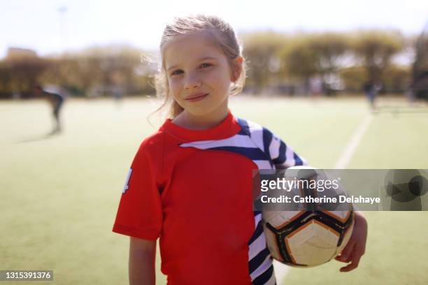 a young girl posing with a ball on a soccer field - playing football fotografías e imágenes de stock
