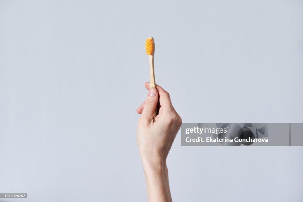 A toothbrush made of natural bamboo material in a woman's hand on a white isolate background.
