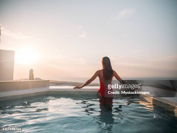 mulher contempla santorini de sua jacuzzi, pôr do sol - infinity pool - fotografias e filmes do acervo
