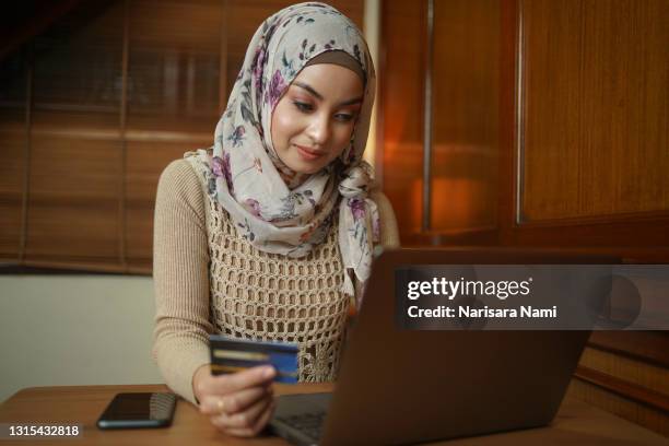 asian muslim woman holding a credit card and using the laptop for online shopping and online payment via the internet. technology concept. - credit score stock pictures, royalty-free photos & images