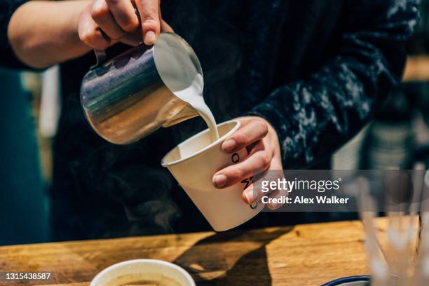 person pouring hot milk from metal jug into coffee cup - takeaway coffee stockfoto's en -beelden