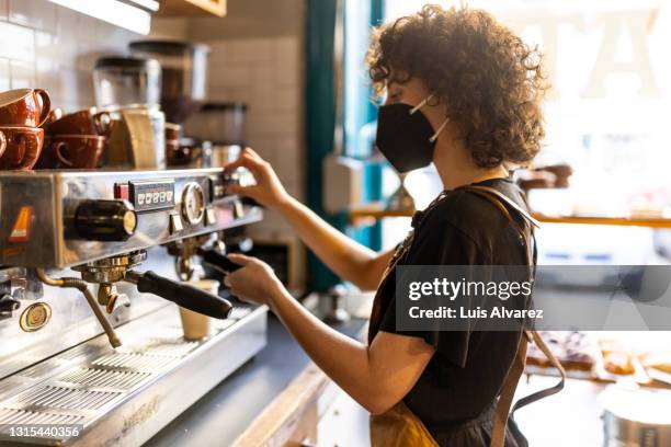 non binary barista wearing a face mask making coffee in a bakery - new business covid stock pictures, royalty-free photos & images