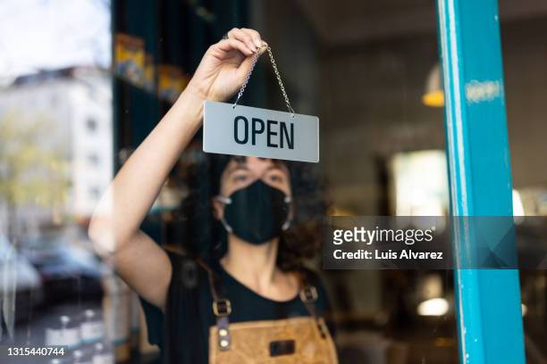 business owner with face mask hanging an open sign at a bakery - inaugurazione foto e immagini stock