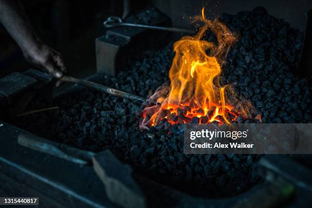 person heating metal in red hot coals using large tongs - blacksmith sparks stock pictures, royalty-free photos & images